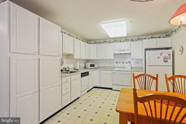 kitchen with a sink, light countertops, white cabinets, under cabinet range hood, and white appliances