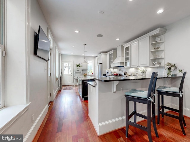 kitchen featuring wall chimney range hood, dark wood-style flooring, high end fridge, white cabinets, and recessed lighting