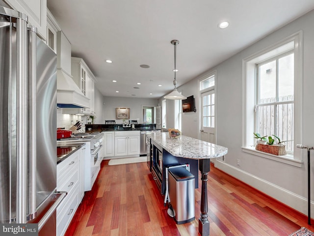 kitchen with appliances with stainless steel finishes, wood finished floors, a peninsula, recessed lighting, and white cabinets