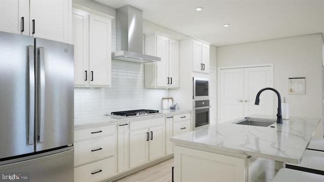 kitchen featuring wall chimney range hood, decorative backsplash, appliances with stainless steel finishes, a sink, and white cabinets