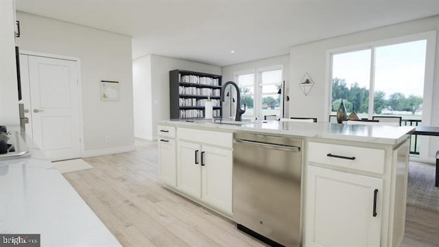 kitchen with stainless steel dishwasher, a center island with sink, light wood finished floors, and white cabinetry