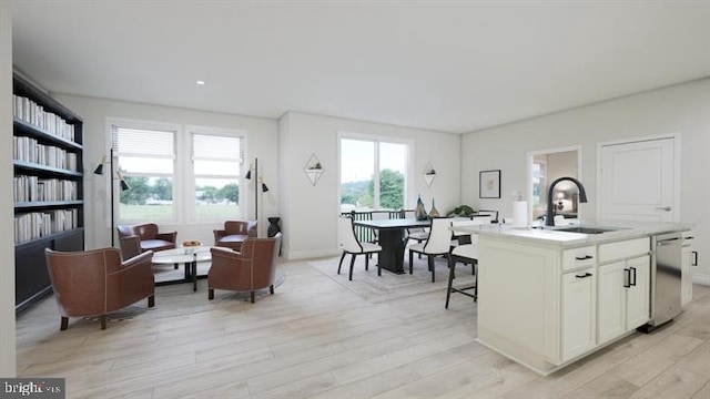 interior space featuring a sink, dishwasher, light countertops, an island with sink, and light wood-type flooring
