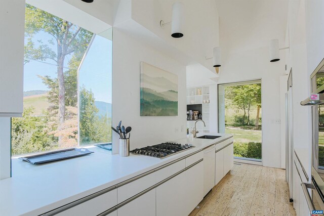 kitchen featuring a healthy amount of sunlight, light countertops, white cabinetry, a sink, and stainless steel gas stovetop