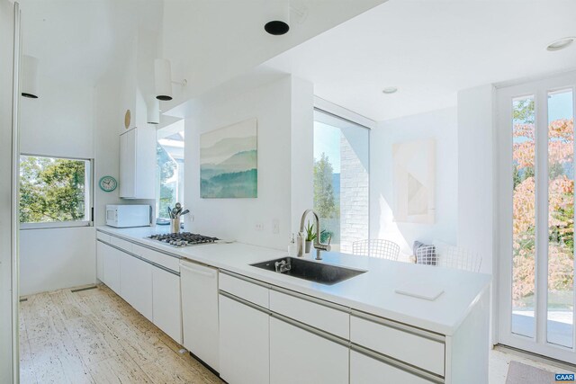kitchen featuring white appliances, light countertops, white cabinetry, a sink, and light wood finished floors