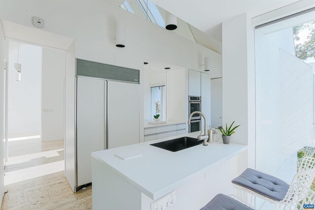 kitchen with a peninsula, stainless steel double oven, light countertops, built in fridge, and a sink