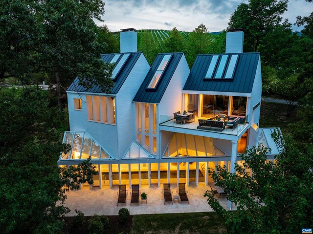 back of house with a patio area, metal roof, a chimney, and a standing seam roof