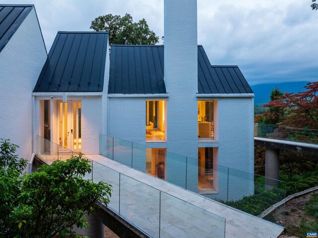 rear view of house with brick siding, a chimney, a balcony, a standing seam roof, and metal roof