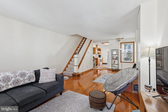 living area with ceiling fan, stairs, and wood finished floors