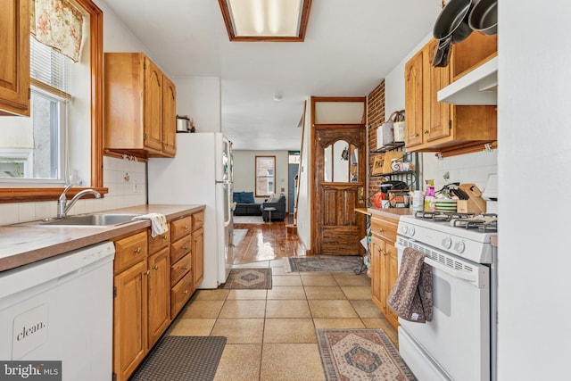 kitchen with light countertops, decorative backsplash, white appliances, and a sink