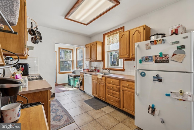 kitchen with decorative backsplash, light tile patterned flooring, white appliances, light countertops, and a sink