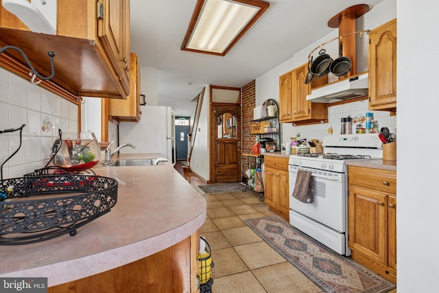 kitchen with decorative backsplash, a sink, light countertops, under cabinet range hood, and white appliances