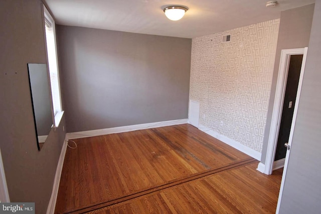 empty room with a wealth of natural light, baseboards, visible vents, and wood finished floors