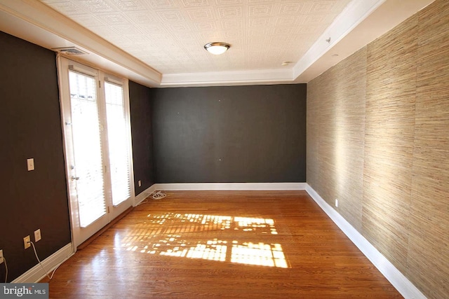 unfurnished room with an ornate ceiling, wallpapered walls, baseboards, an accent wall, and wood finished floors