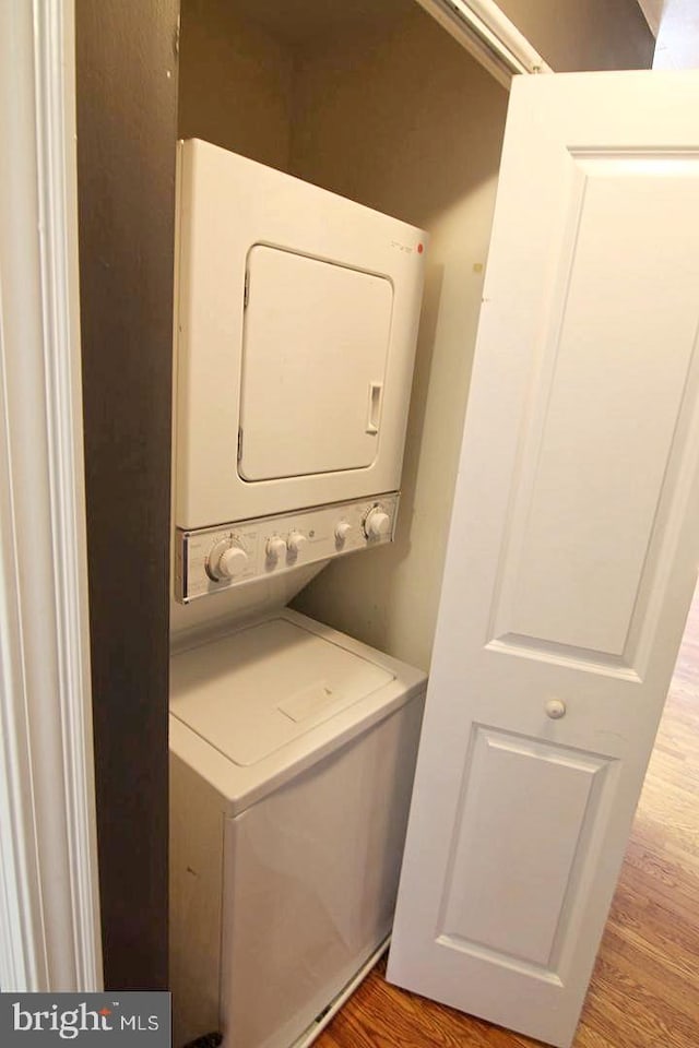 laundry room featuring laundry area, stacked washer / drying machine, and wood finished floors