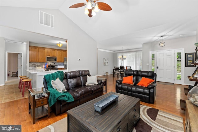 living room with vaulted ceiling, ceiling fan with notable chandelier, light wood-type flooring, and visible vents