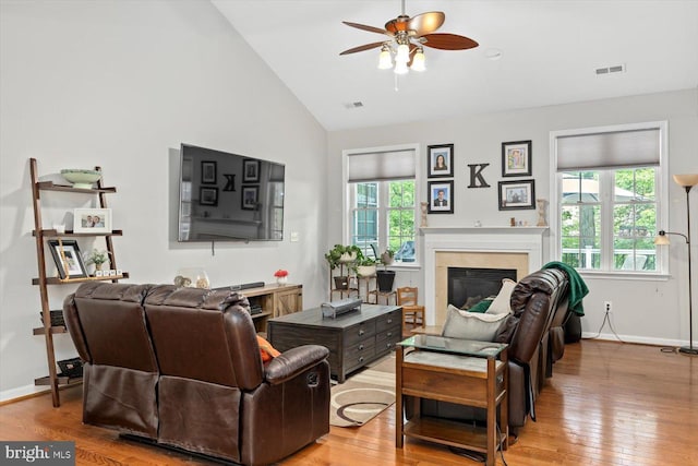 living area featuring ceiling fan, visible vents, a glass covered fireplace, and wood finished floors