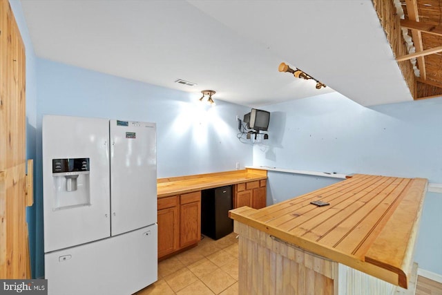 kitchen with white refrigerator with ice dispenser, butcher block countertops, a peninsula, light tile patterned floors, and refrigerator