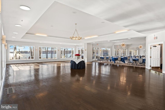 interior space with visible vents, a chandelier, wood finished floors, and a raised ceiling