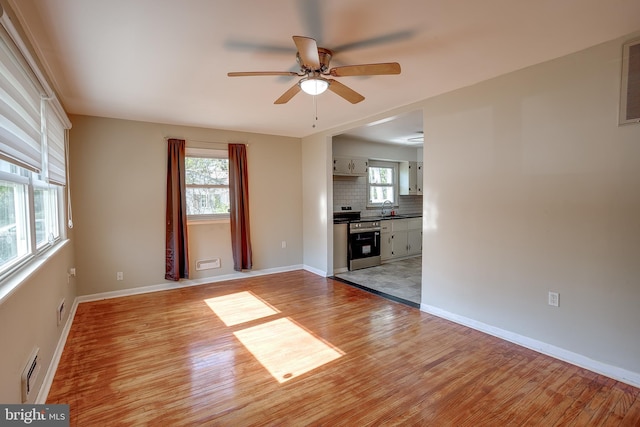 unfurnished living room featuring baseboards, a sink, light wood finished floors, and ceiling fan