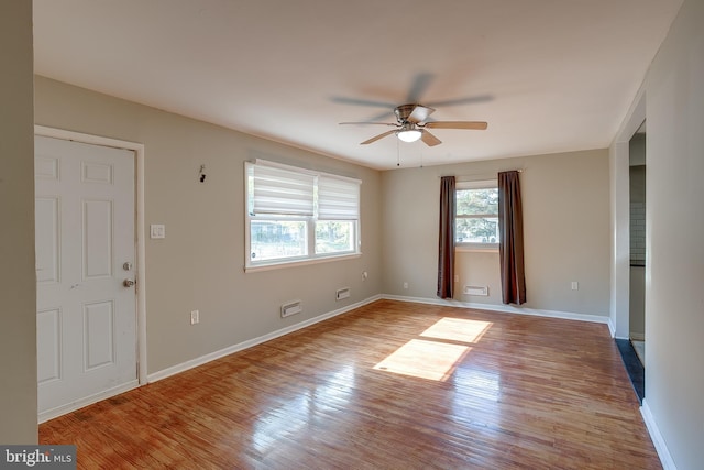 interior space with baseboards, a ceiling fan, wood finished floors, and visible vents