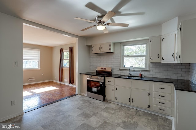 kitchen with a ceiling fan, stainless steel range with electric stovetop, dark countertops, a sink, and backsplash