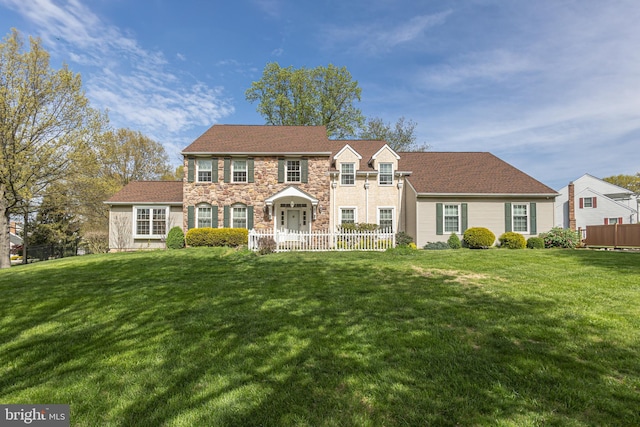 colonial inspired home with fence, a front yard, and stone siding