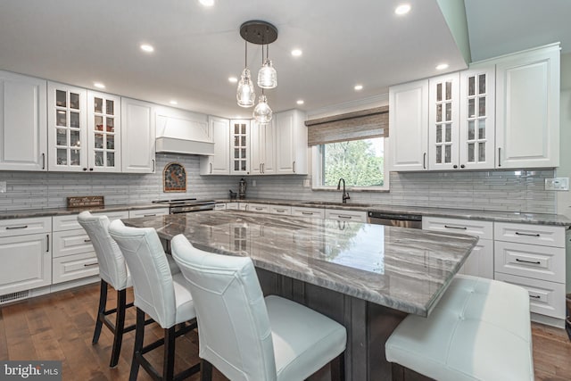 kitchen featuring custom exhaust hood, a kitchen island, white cabinets, a sink, and range