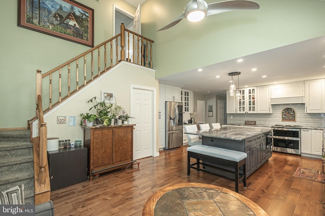 kitchen with dark wood-style flooring, stainless steel appliances, white cabinetry, decorative backsplash, and a kitchen island