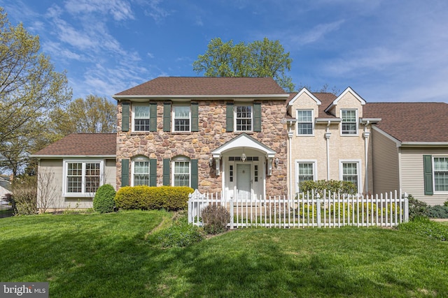 colonial home with a front yard, fence private yard, and stone siding
