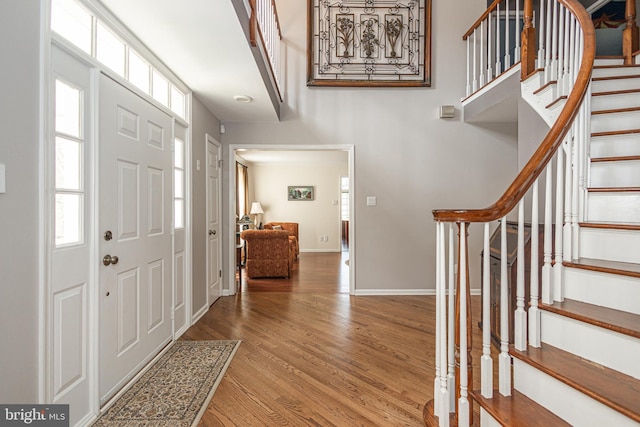 entryway featuring stairs, baseboards, a healthy amount of sunlight, and wood finished floors
