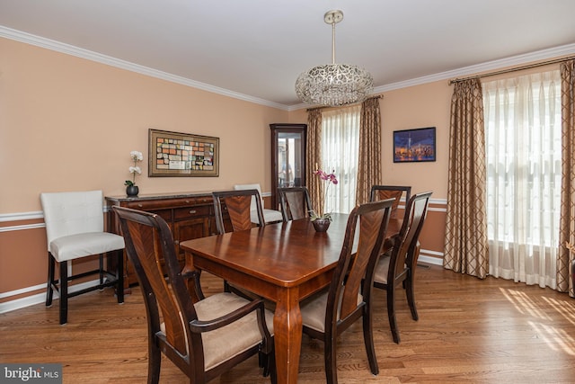 dining space with light wood-style floors, baseboards, ornamental molding, and a notable chandelier