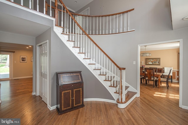 stairway with baseboards, wood finished floors, and a towering ceiling