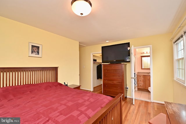 bedroom with a closet, baseboards, a walk in closet, light wood-style flooring, and ensuite bath