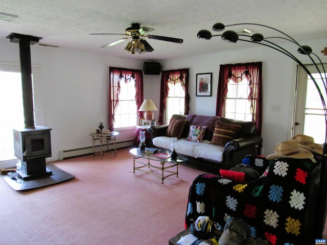 carpeted living room with ceiling fan, plenty of natural light, a wood stove, and a baseboard radiator