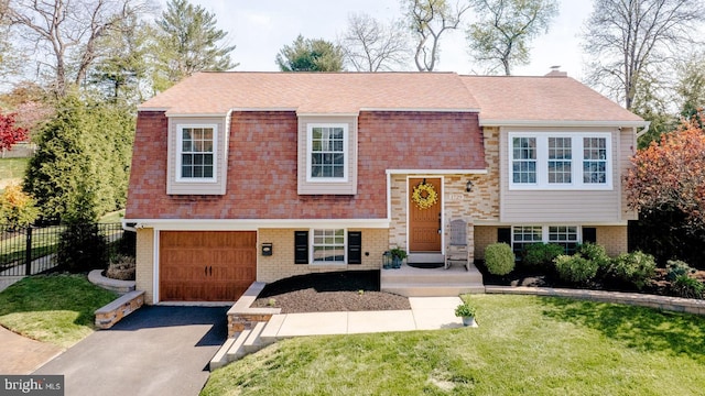 bi-level home featuring a garage, fence, a front yard, roof with shingles, and driveway