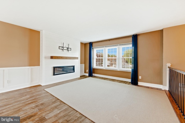 unfurnished living room featuring wainscoting, wood finished floors, and a fireplace