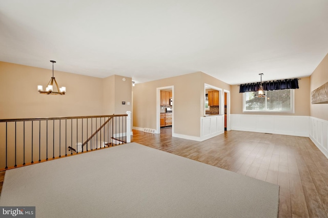unfurnished room with a wainscoted wall, wood finished floors, and a chandelier