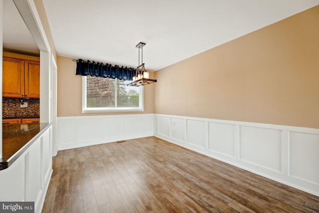 unfurnished dining area featuring visible vents, a wainscoted wall, a chandelier, a decorative wall, and light wood-style flooring
