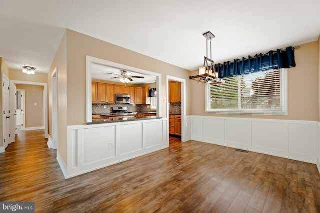 kitchen with dark countertops, appliances with stainless steel finishes, brown cabinetry, decorative backsplash, and wood finished floors