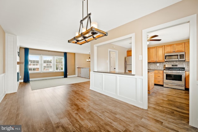 kitchen featuring decorative backsplash, open floor plan, light wood-type flooring, ceiling fan with notable chandelier, and stainless steel appliances