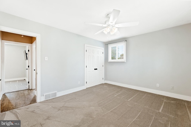 carpeted spare room featuring visible vents, a ceiling fan, and baseboards