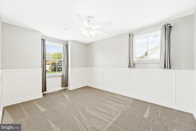 spare room featuring a wainscoted wall, ceiling fan, and carpet