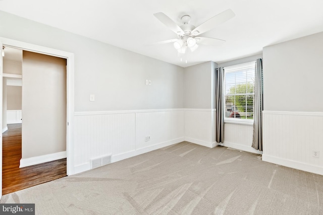 spare room featuring ceiling fan, visible vents, and wainscoting