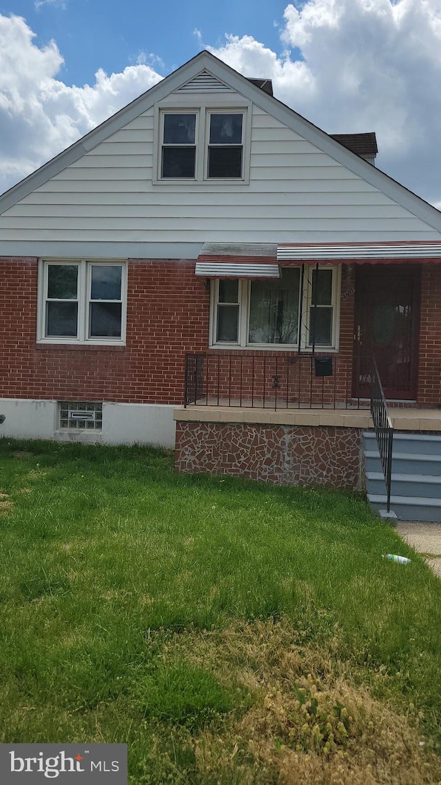 view of side of property with brick siding, a yard, and covered porch