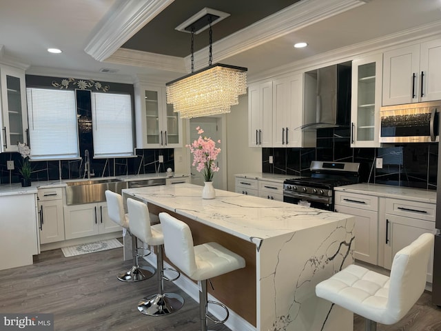 kitchen featuring crown molding, white cabinetry, wall chimney range hood, and stainless steel appliances