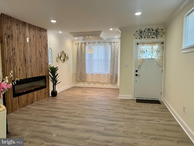 foyer entrance with crown molding, wood finished floors, baseboards, a glass covered fireplace, and recessed lighting