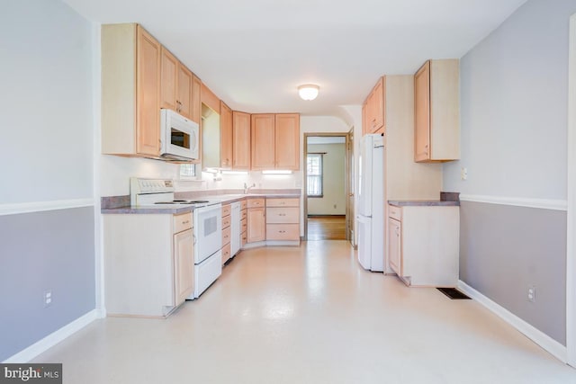 kitchen featuring baseboards, a sink, light brown cabinetry, and white appliances