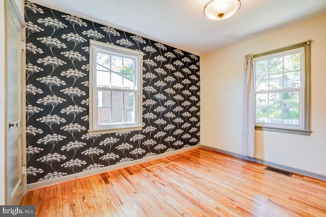 spare room with wallpapered walls, visible vents, baseboards, and hardwood / wood-style floors
