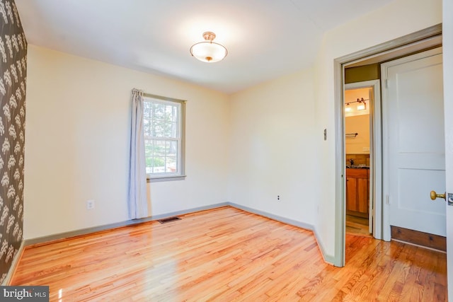 empty room featuring visible vents, light wood-style floors, and baseboards
