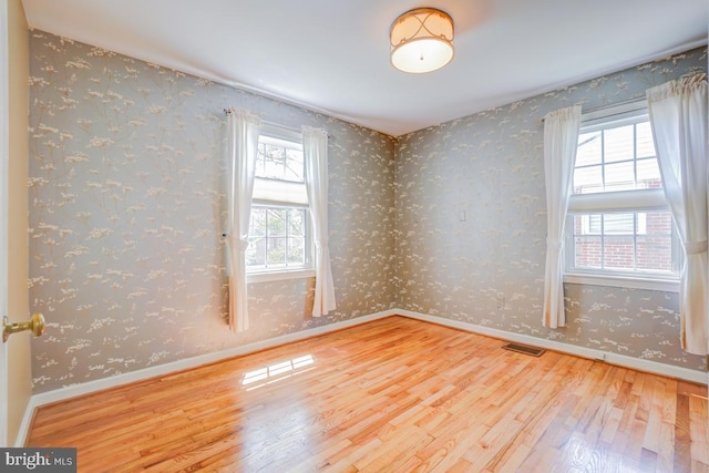 spare room with baseboards, wood finished floors, and wallpapered walls